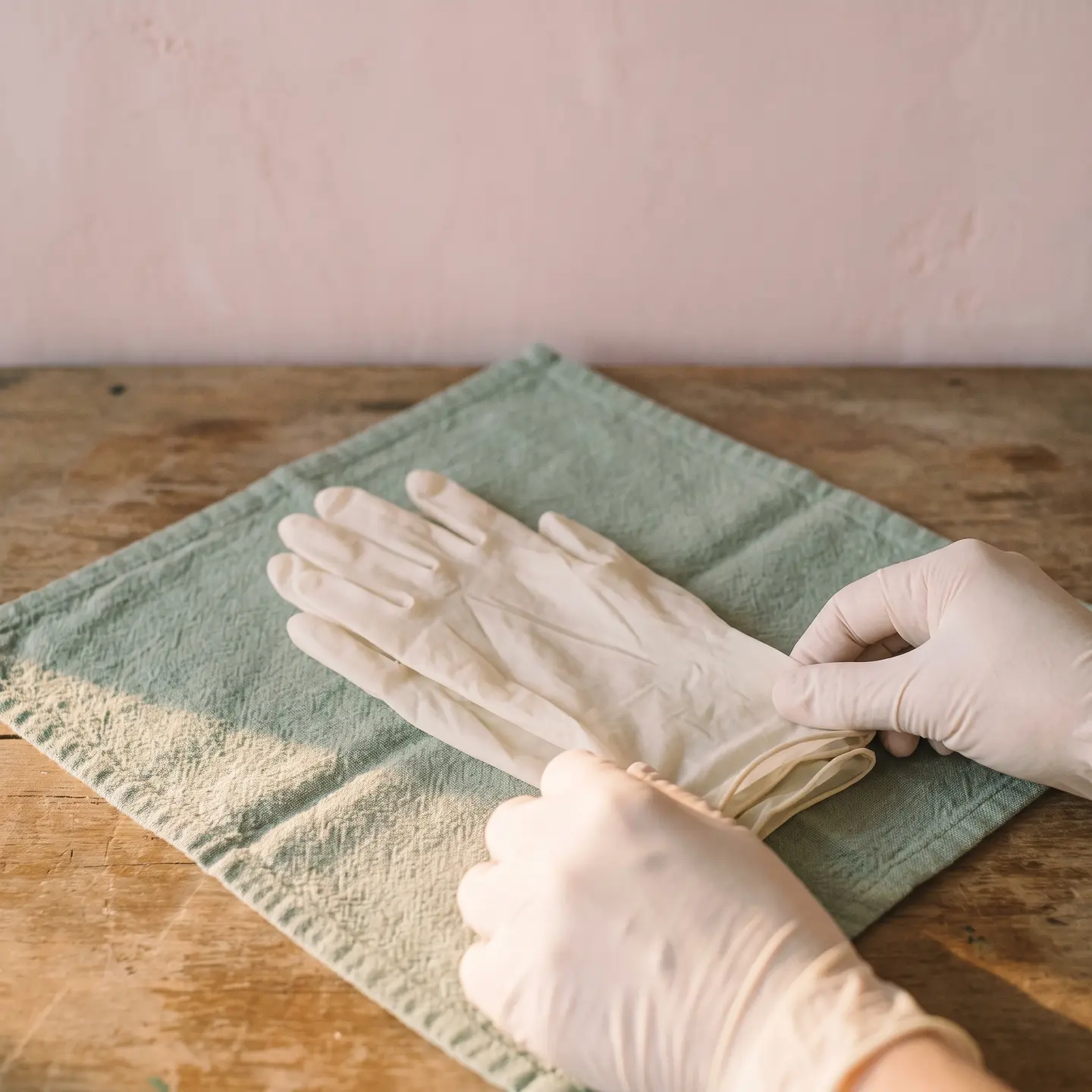 Par de guantes de nitrilo claros doblados sobre un paño verde salvia