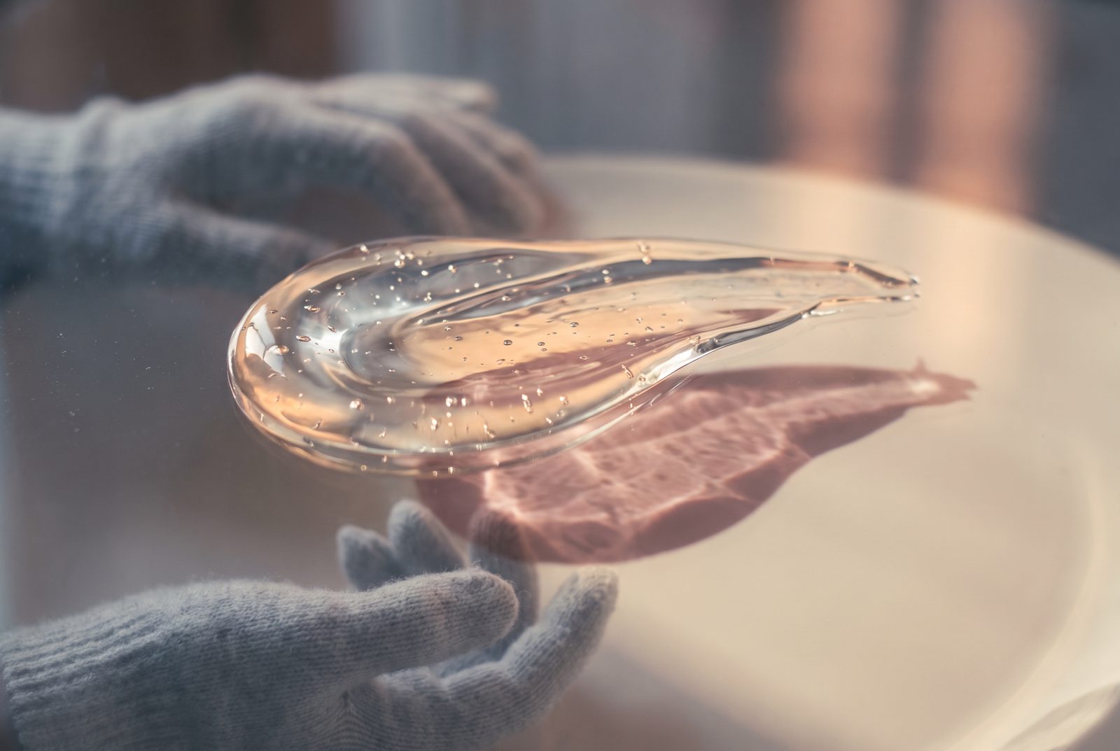 Gel transparente extendido sobre vidrio con pequeñas burbujas, bajo luz lateral cálida
